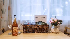 A table with a bottle of wine, glasses, a wicker basket, a welcome sign, and a vase with flowers. - Little Blue Cottage - wooded getaway, near beaches and towns (Benton Harbor)