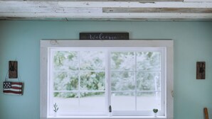 A window with a 'welcome' sign above it, a small cactus, and a flag on the wall. - Little Blue Cottage - wooded getaway, near beaches and towns (Benton Harbor)