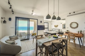 Ein modernes Wohnzimmer mit Sofa, Esstisch und Stühlen, ein Balkon mit Aussicht sowie ein Schlafzimmer mit Bett und Schreibtisch.