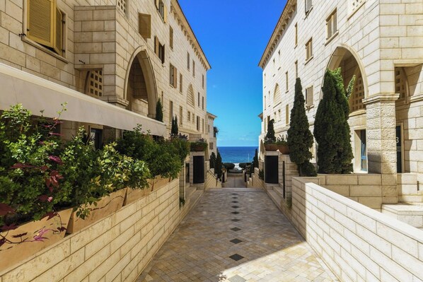 A stone pathway leading to a building with arched windows and a view of the sea.
