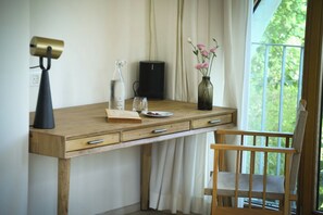 Un bureau en bois, une lampe, une bouteille en verre, un haut-parleur et un vase rempli de fleurs.