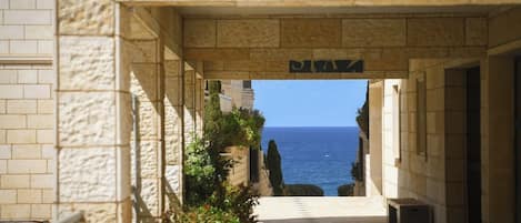 A stone corridor leading to a view of the sea, with a sign above the entrance.