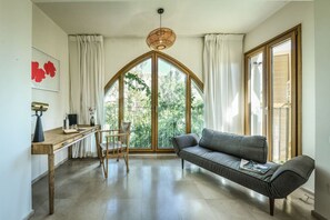 A room with a wooden desk, a grey sofa, a chair, and a large window with curtains. - Mamad Breathtaking 3 BR Apt w Sea View in Central (Tel Aviv-Yafo)