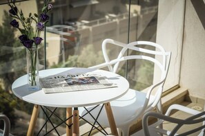 Ein runder, weißer Tisch mit einer Zeitung, einer klaren Vase mit violetten Blumen und einem weißen Stuhl.