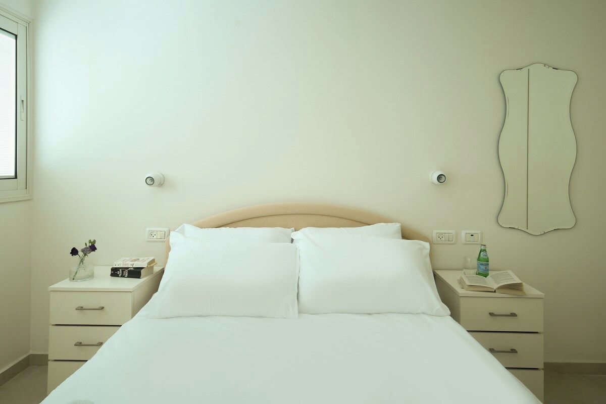 Une chambre à coucher avec un lit, deux tables de chevet, un miroir et une fenêtre.