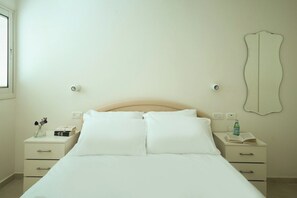 Une chambre à coucher avec un lit, deux tables de chevet, un miroir et une fenêtre.
