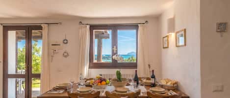 A dining area with a table set for six, a view of the outdoors, and a window with curtains.