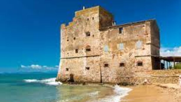 A stone building with a tower, situated by the sea. - Bedo House - Beachfront Sea View Apartment in Follonica, Follonica, Italy (Follonica)
