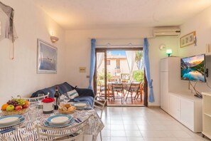 Un comedor con una mesa lista para dos personas, un sofá, un televisor y vistas al exterior.
