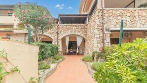 A courtyard with a stone wall, a table with chairs, and a hanging plant. - I Fari 77 600m From The Beach, Porto San Paolo, Italy (Porto San Paolo)