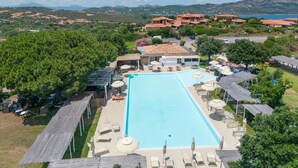 A large rectangular pool with lounge chairs and umbrellas, surrounded by buildings and trees. - I Fari 77 600m From The Beach, Porto San Paolo, Italy (Porto San Paolo)