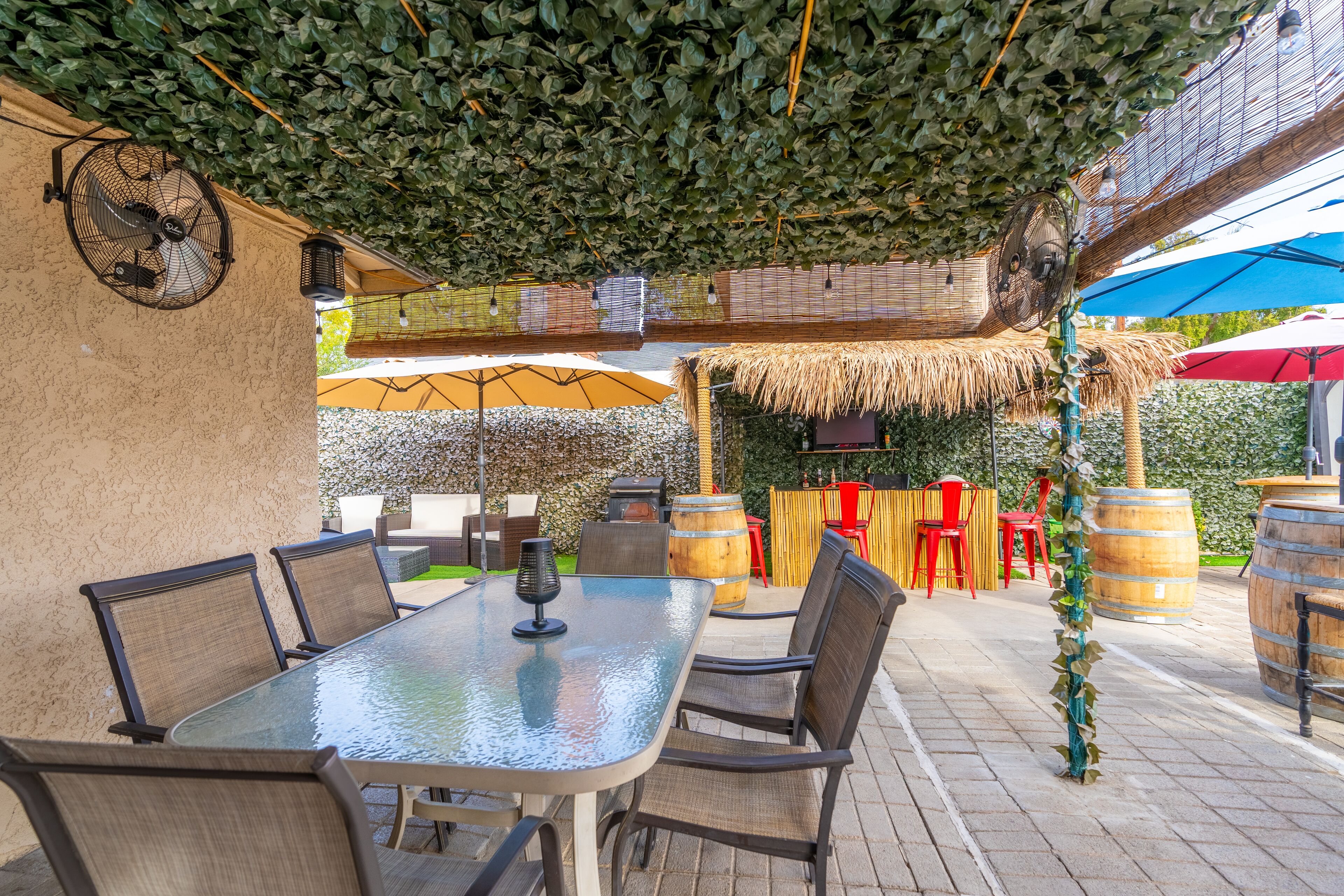 An outdoor patio area with a glass-top table, chairs, and a thatched umbrella.