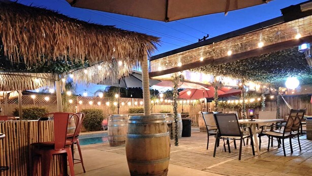 An outdoor patio area with tables and chairs, a pool, and decorative lighting. - Tropical Paradise  (Fresno)
