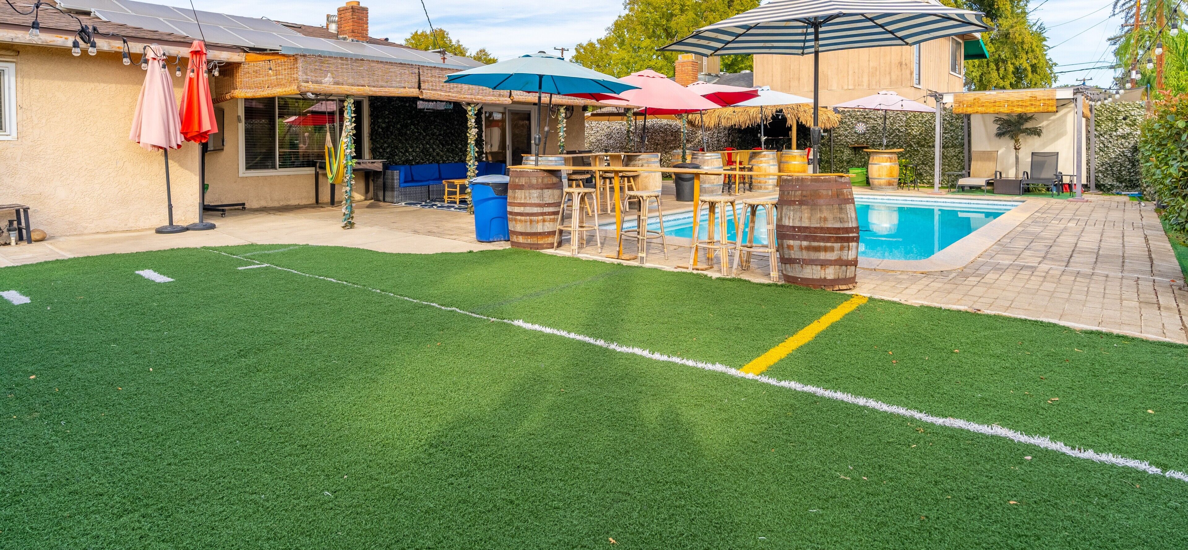 Um quintal com grama sintética, piscina, área de estar externa e um bar.