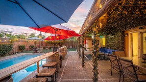 A poolside area with umbrellas, seating, and a stone wall. - Tropical Paradise  (Fresno)