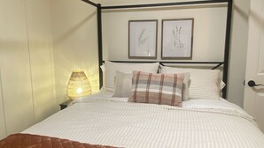 A neatly made bed with a brown quilt, white pillows, and two framed botanical prints on the headboard.