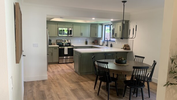 A modern kitchen with light green cabinets, a central island, and a dining area with black chairs.