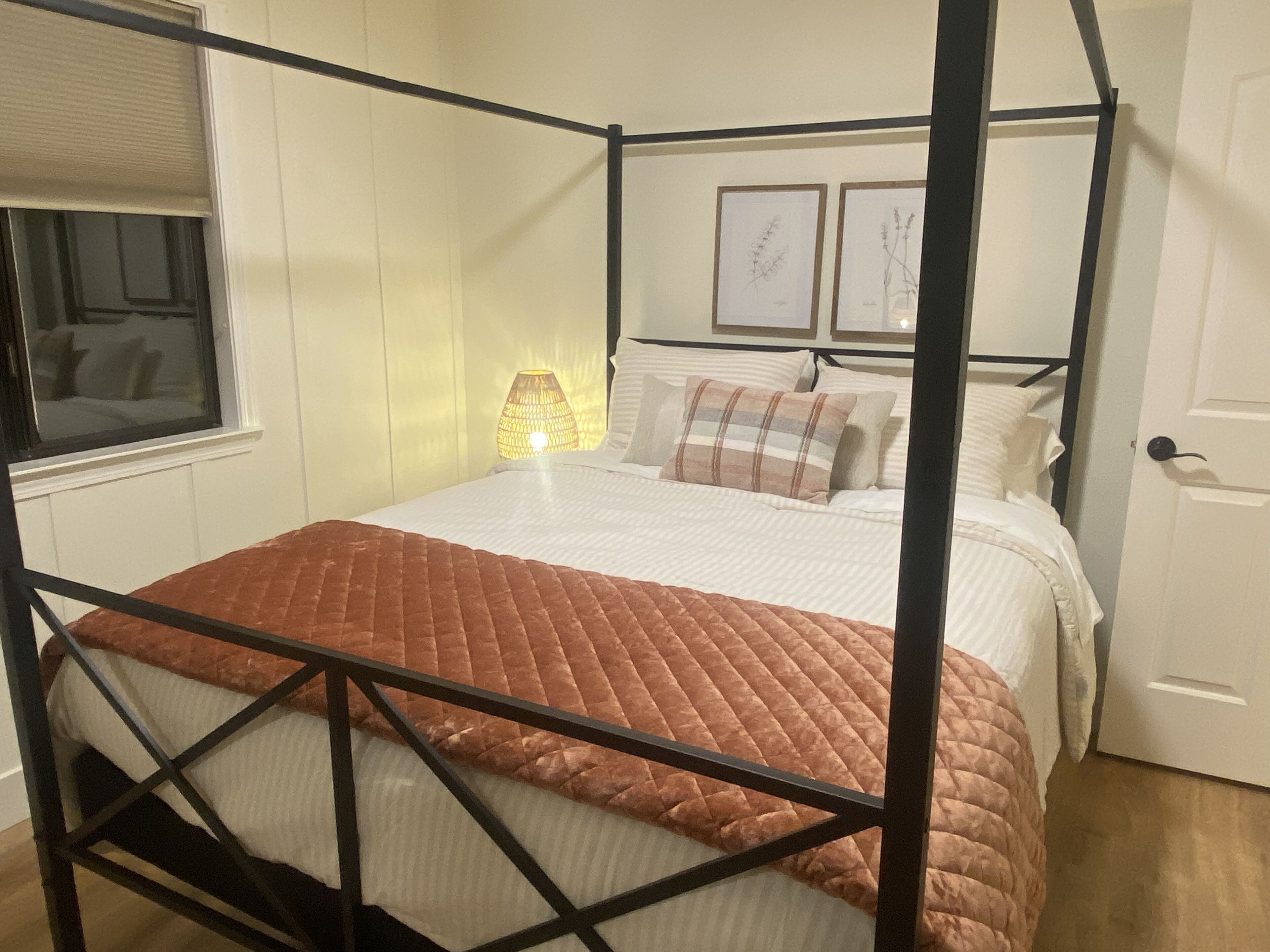 A four-poster bed with a brown quilt, white bedding, and a bedside lamp.