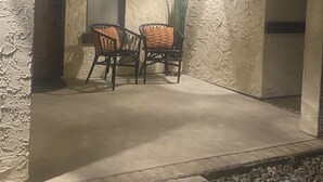 An outdoor patio area with two wicker chairs and a table, a potted plant, and a wall-mounted light fixture.