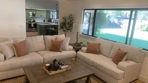 A living room with a beige sectional sofa, a wooden coffee table, and a view of a backyard through a large window.