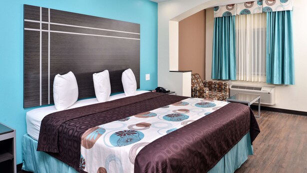 Ein Hotelzimmer mit einem großen Bett, einem Nachttisch, einem Sessel und einem Fenster mit Vorhängen.