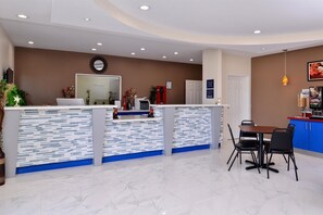 Un'area reception dal design moderno, con una scrivania, un angolo salotto con tavolo e sedie, e un bancone con zoccolo a motivi blu e bianchi.