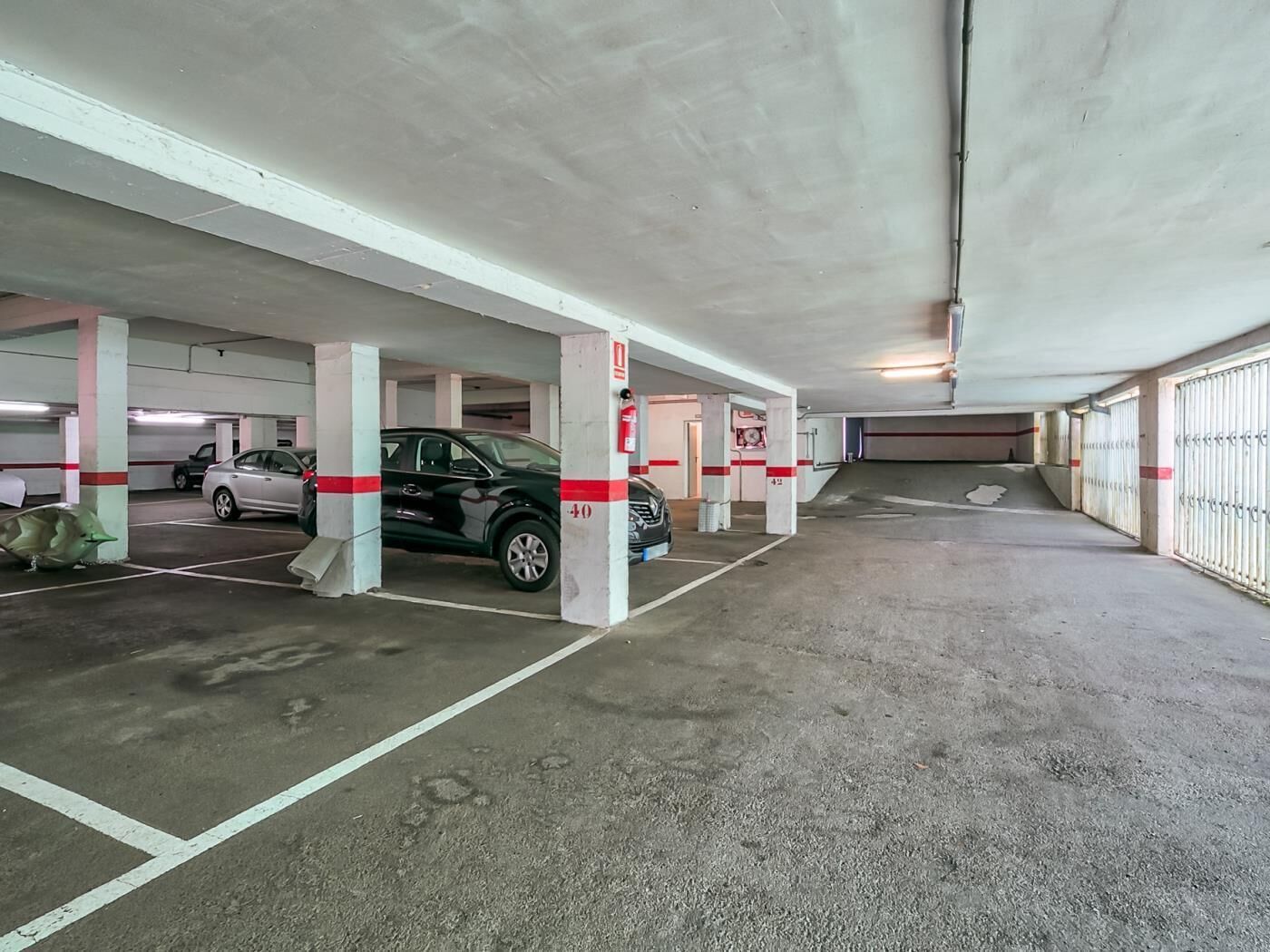 Un parking à plusieurs niveaux, doté de piliers en béton et de places de stationnement délimitées.