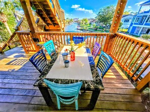 Eine Holzdielen-Terrasse mit Tisch und Stühlen mit Blick auf ein Gewässer und Gebäude.