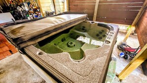 Un bain à remous avec un couvercle, un banc en bois et un sol en béton.