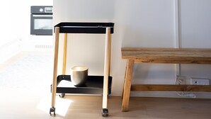 Un salon moderne avec un téléviseur à écran plat fixé au mur, un banc en bois et une petite table sur roulettes.