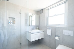 Ein modernes Badezimmer mit einer Duschkabine aus Glas, einem weißen Waschbecken und einem großen Spiegel.