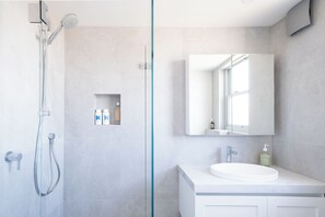 Een moderne badkamer met een douchecabine van glas, een witte wastafel en een grote spiegel.