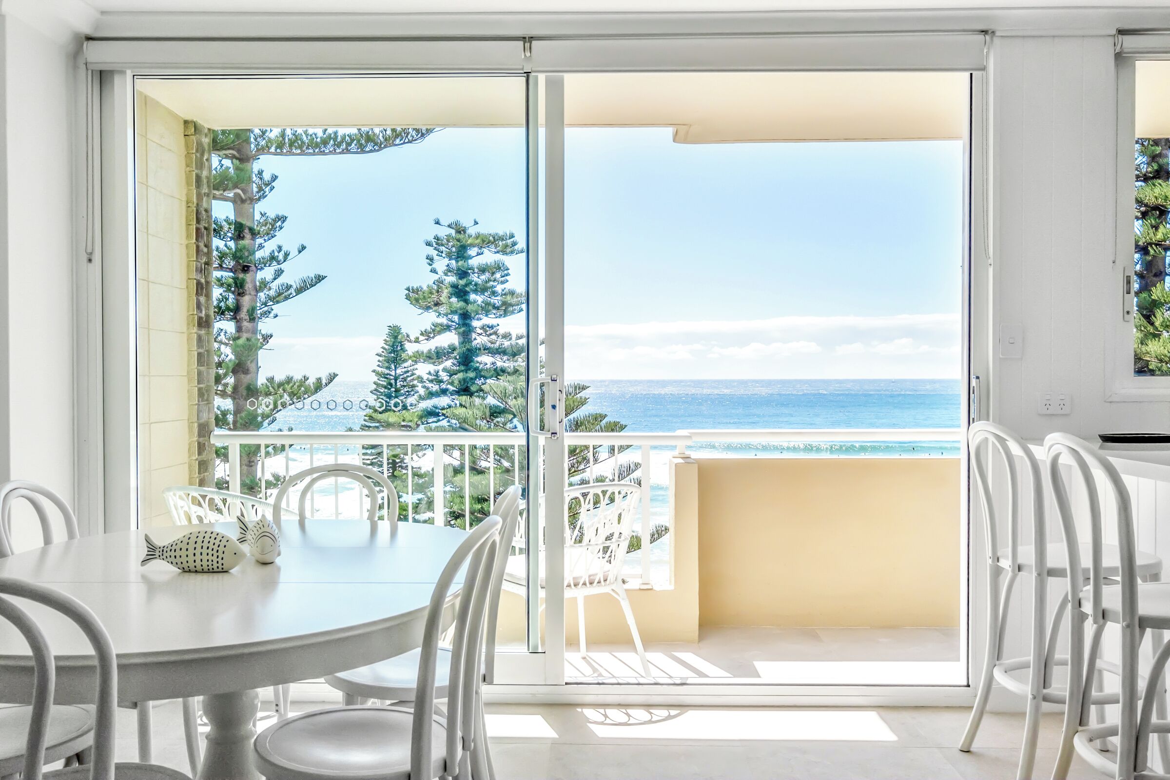A dining area with a table and chairs, a view of the sea, and a balcony with a railing.