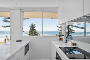 A modern kitchen with a view of the ocean, featuring white cabinetry, a built-in oven, and a coffee maker.