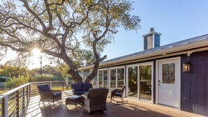 Une terrasse en bois avec des meubles d’extérieur, une porte vitrée et une cheminée en métal.