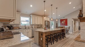 Une cuisine moderne dotée d’un îlot central, d’appareils électroménagers en acier inoxydable et de luminaires suspendus.