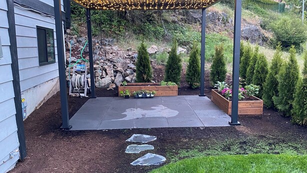 Un patio cubierto con pérgola, escalones de piedra y un jardín con plantas en macetas y arbustos.