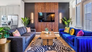 A modern living room with a sofa, a coffee table, and a TV mounted on a wooden wall. - Urban Jungle Retreat in the HTX Skyline (Houston)