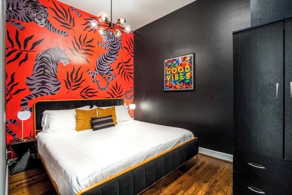 Un dormitorio con una cama, una mesita de noche, un armario y una pared con estampado de hojas y un tigre.
