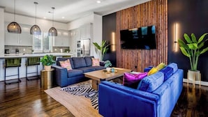 A modern living room with a blue sofa, a wooden accent wall, and a flat-screen TV. - Urban Jungle Retreat in the HTX Skyline (Houston)