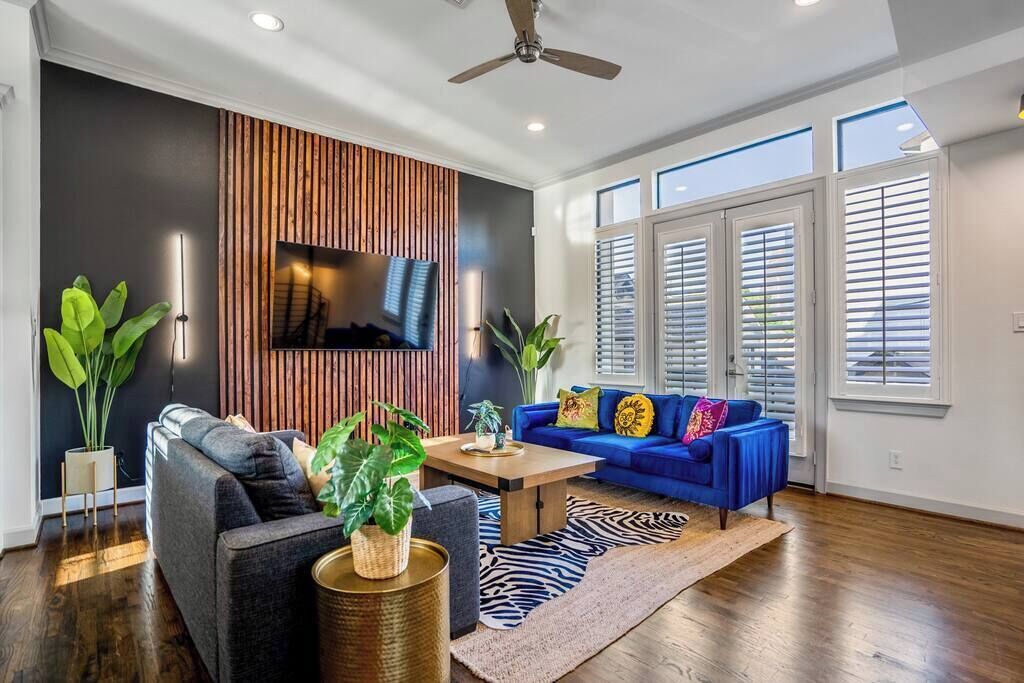 A modern living room with a blue sofa, a grey armchair, a wooden coffee table, and a TV mounted on a wooden panel wall.