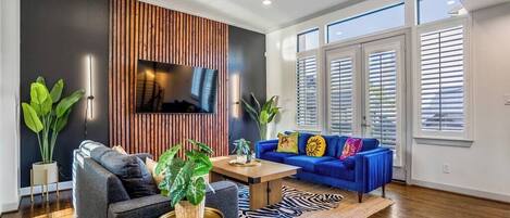 A modern living room with a blue sofa, a grey armchair, a wooden coffee table, and a TV mounted on a wooden panel wall.