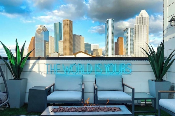 Large rooftop deck with stunning views overlooking downtown HTX. Features a fire place, custom neon sign, 3 seater sofa, 2 seater love seat, 2 single chairs, and one suspended egg chair.