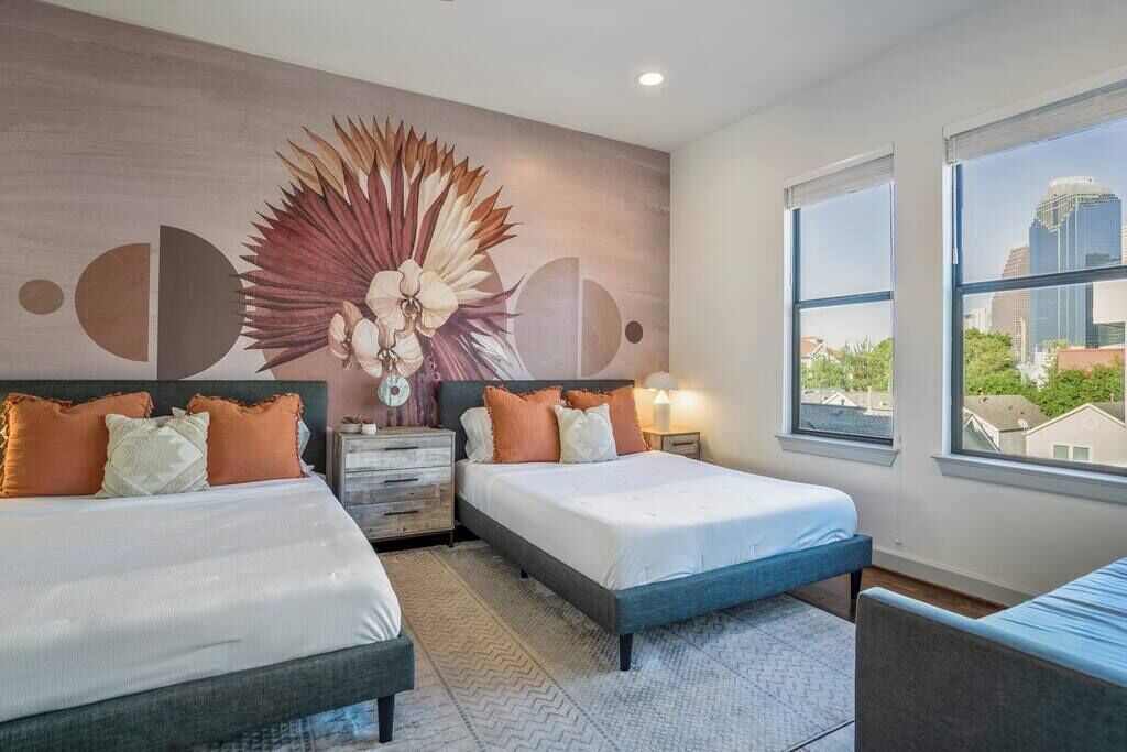 Quarto de hotel moderno com duas camas, um mural grande na parede e vista da cidade pela janela.