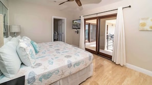 A bedroom with a bed, a ceiling fan, a door leading to a balcony, and a view of the outside.