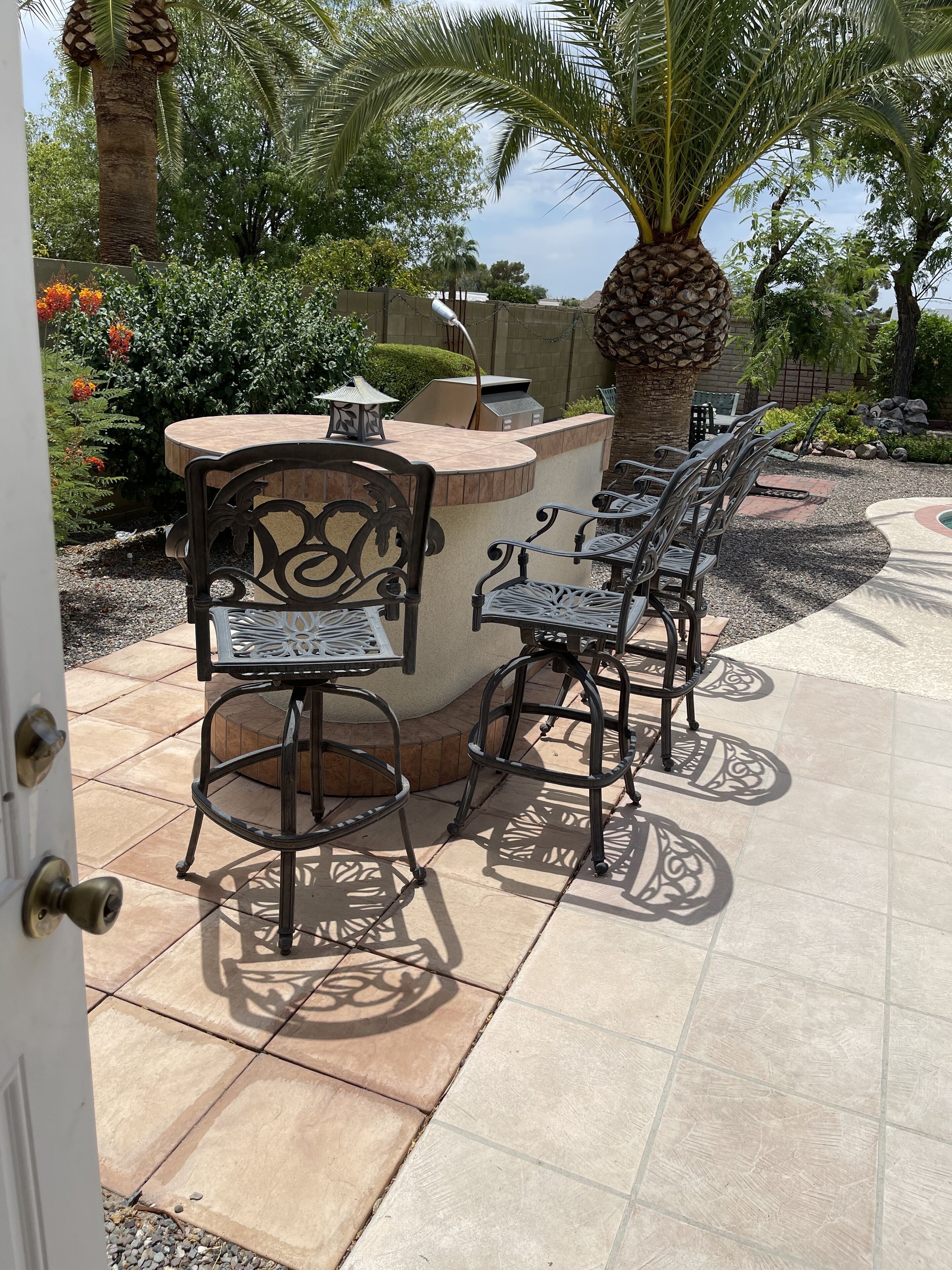 An outdoor patio with a bar area, two metal chairs, a table, and a palm tree.