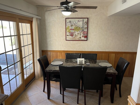 A dining area with a table set for four, a ceiling fan, and a wall-mounted picture of a bistro scene.