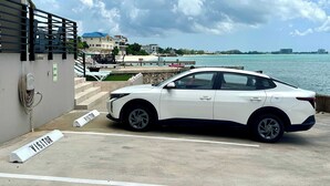 Ein weißes Auto steht auf einem Besucherparkplatz mit Blick auf das Meer und Gebäude im Hintergrund.