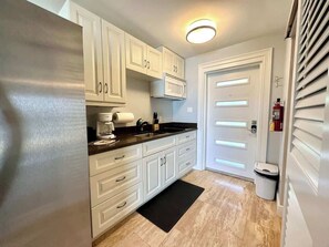 A kitchen with white cabinets, a black countertop, and a black rug.