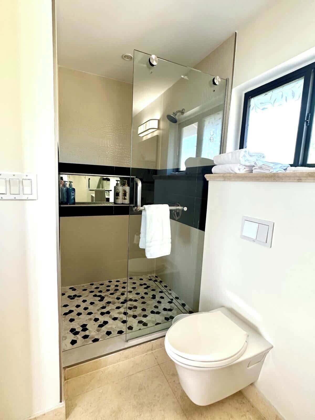 A modern bathroom with a glass-enclosed shower, a toilet, and a sink area.